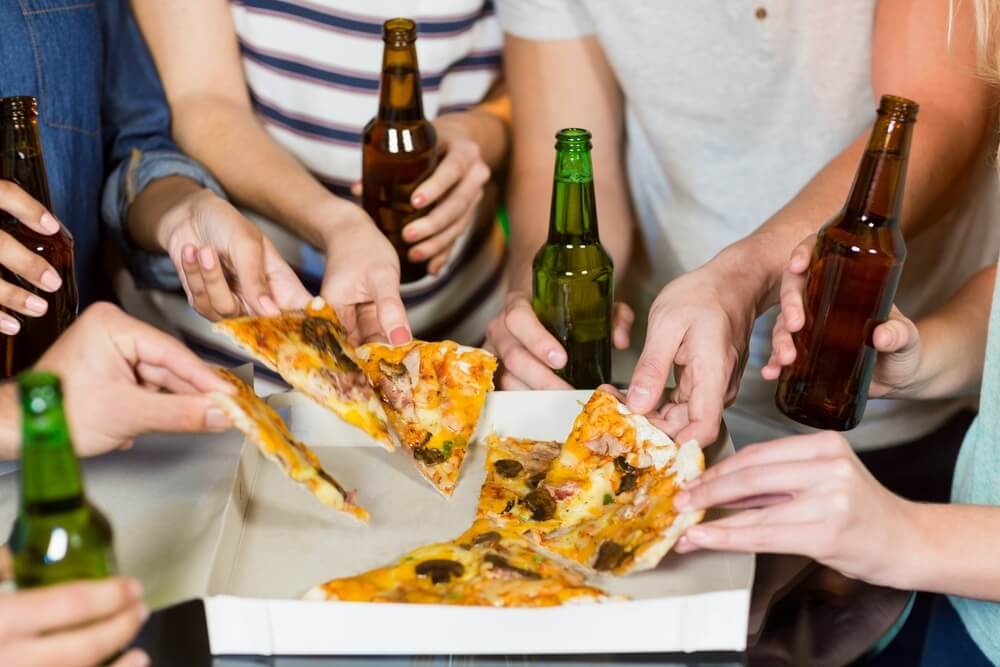Mid section of friends having bottle of beer and pizza in party at bar