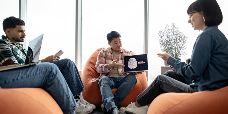 Man sits on beanbag chair in startup office while presenting on his laptop 