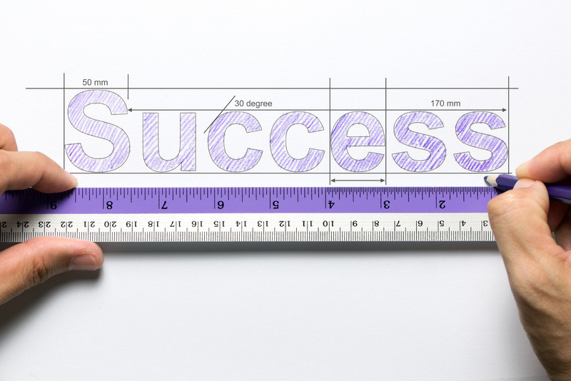 A person draws the word "success" using a ruler as a measurement guide